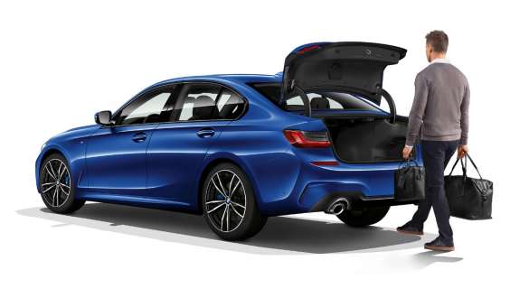 BMW 3 Series Sedan,自動尾門系統 BMW 3 Series Sedan Sport 系列後側四分之三角度影像,駕駛者正在用腳自動開啟尾門。