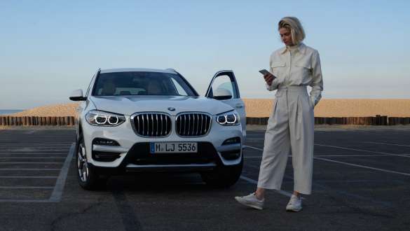 My BMW 應用程式 BMW 女模特拿著智慧型手機站在一輛 BMW 前 My BMW 應用程式 BMW 女模特拿著智慧型手機站在一輛 BMW 前