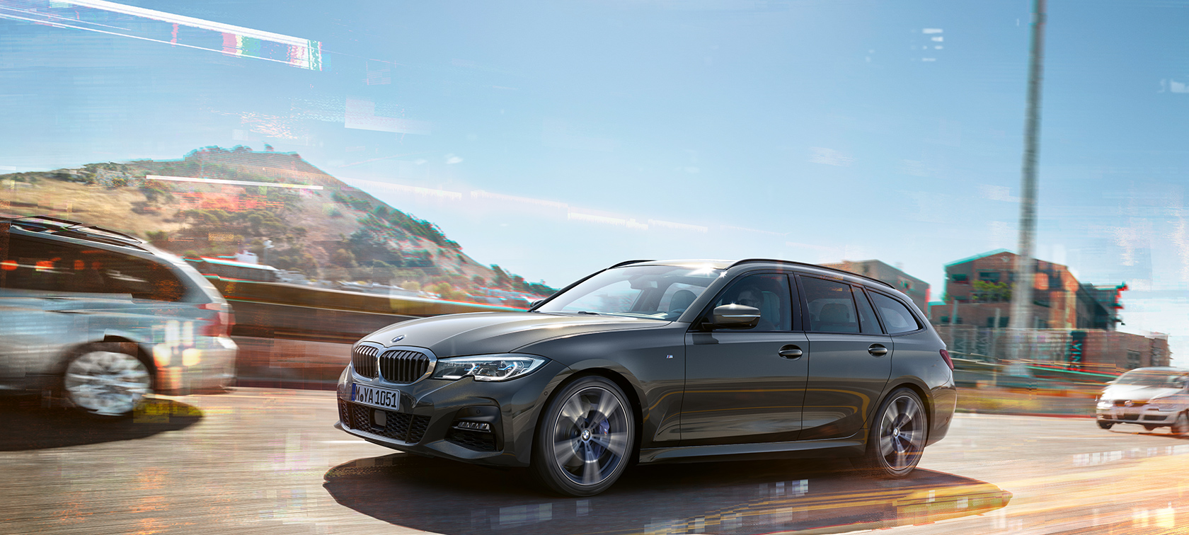 BMW 3 Series Touring, lateral driving shot in front of houses and mountains in the background