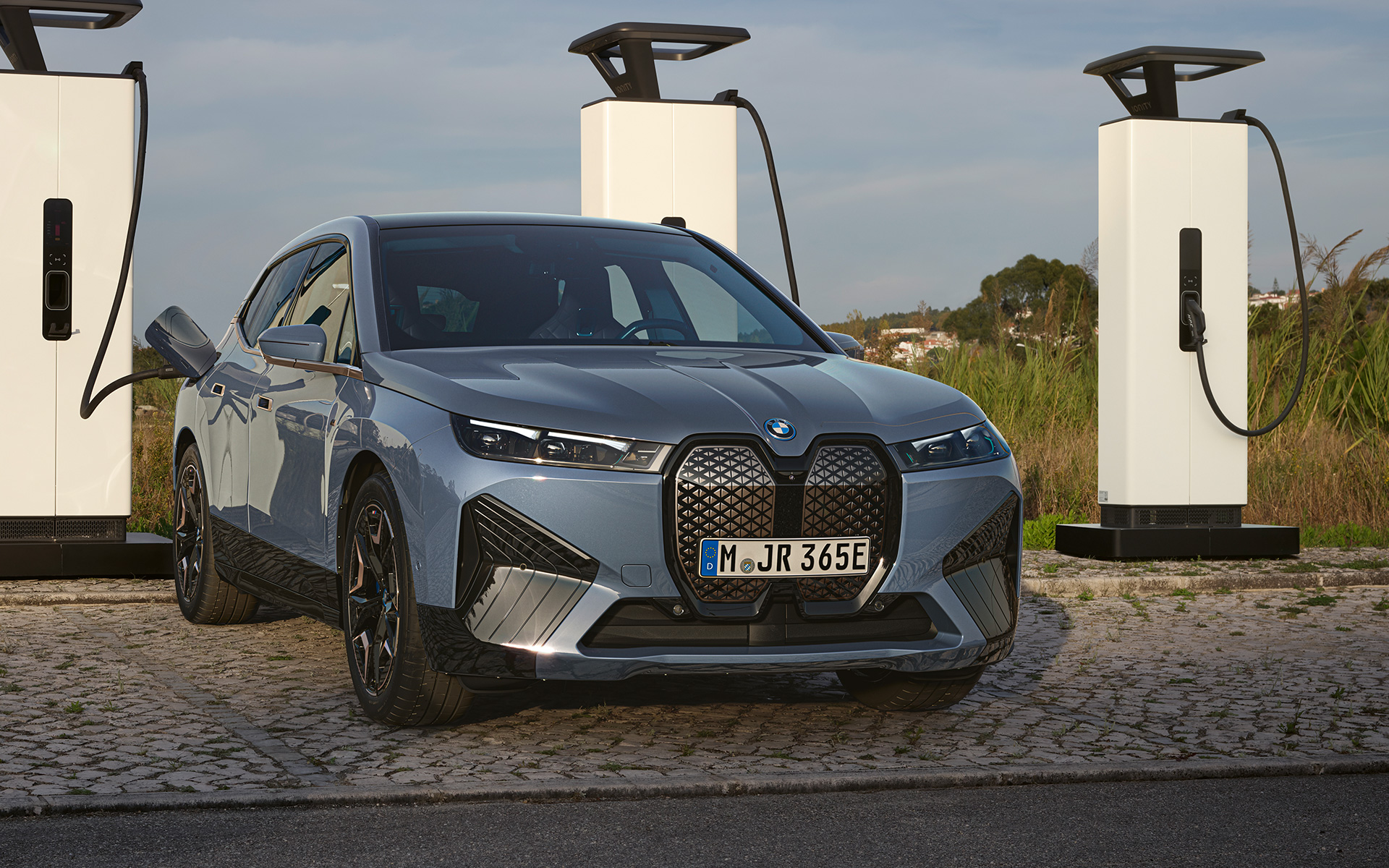 Front view BMW iX M60 i20 2022 electric SUV BMW Individual Storm Bay metallic at high-power charging station BMW iX M60 i20 2022 electric SUV BMW Individual Storm Bay metallic front view at high-power charging station