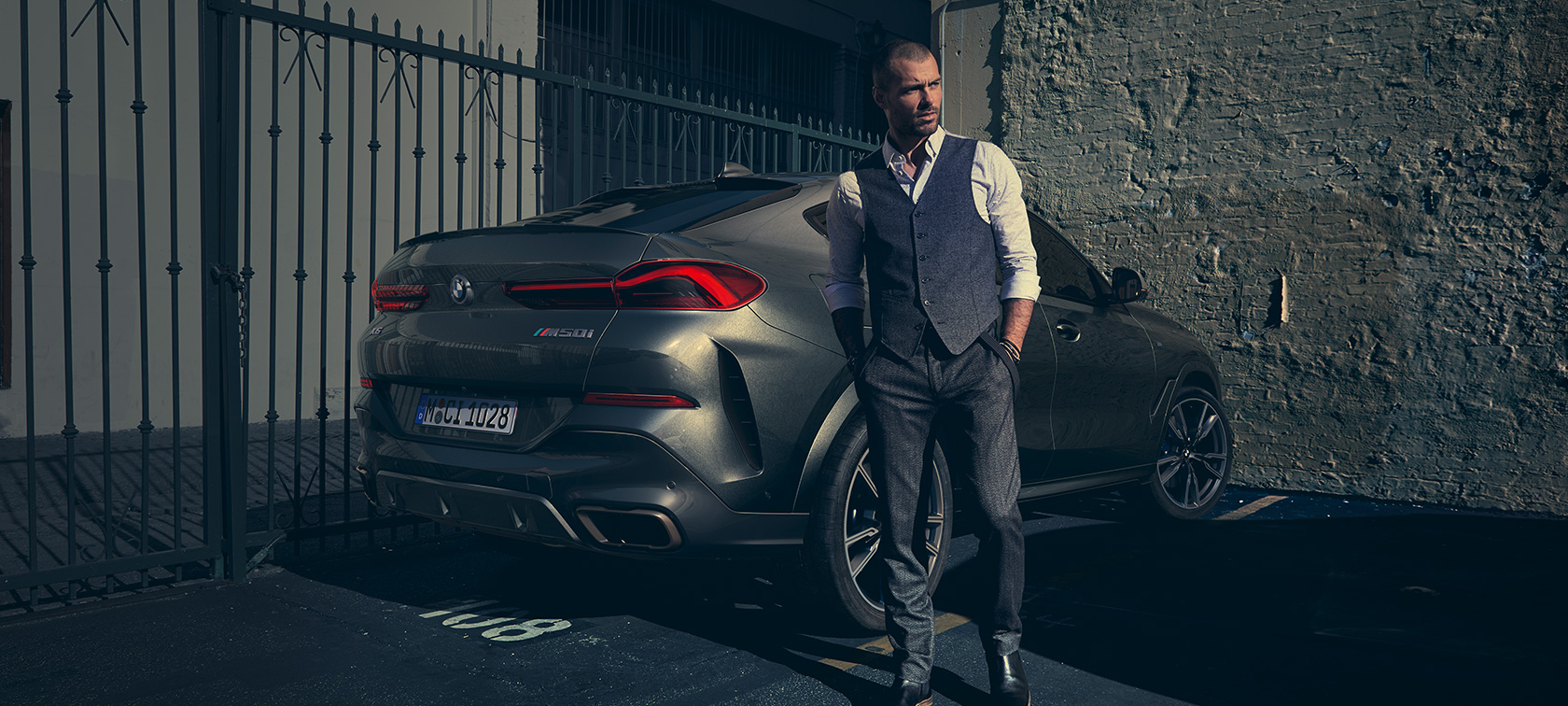 BMW X6 M50i in three-quarter rear view Man standing next to BMW X6 M50i SUV in three-quarter rear view
