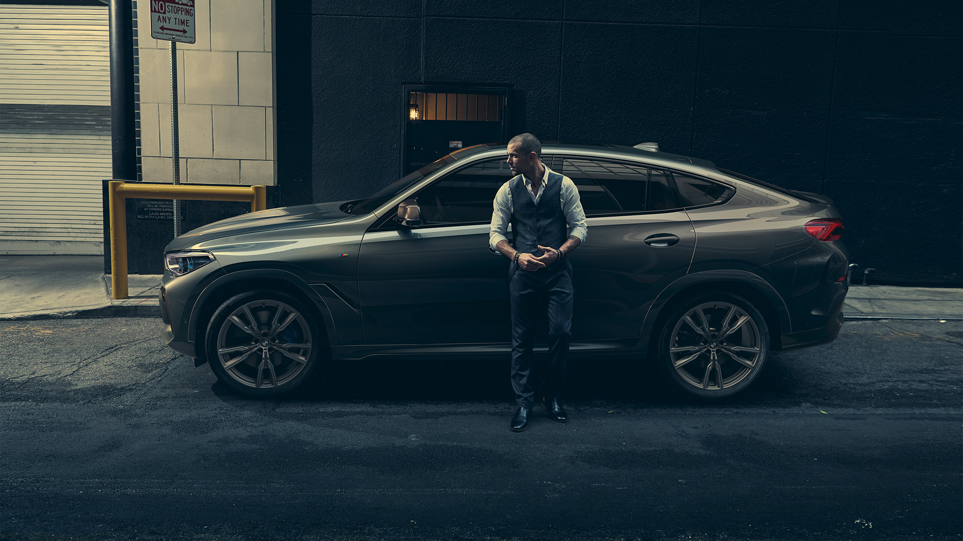 BMW X6 M50i,側面視角 一名男士斜靠在 BMW X6 M50i 上,側面視角,背景為都市環境