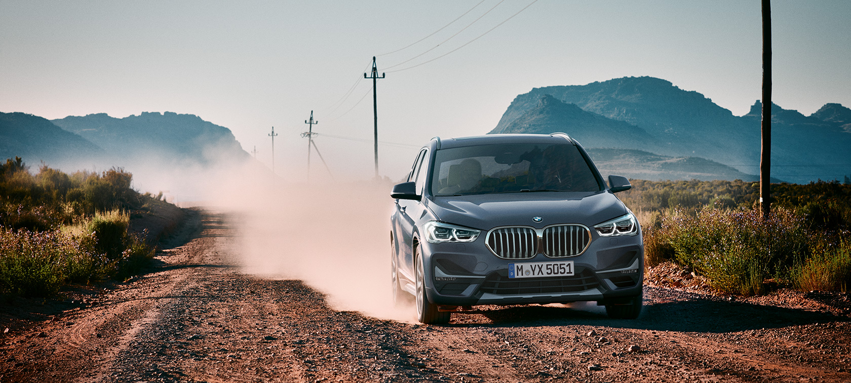 BMW X1, three-quarter rear view. BMW X1, three-quarter rear view driving in front of mountain scenery.