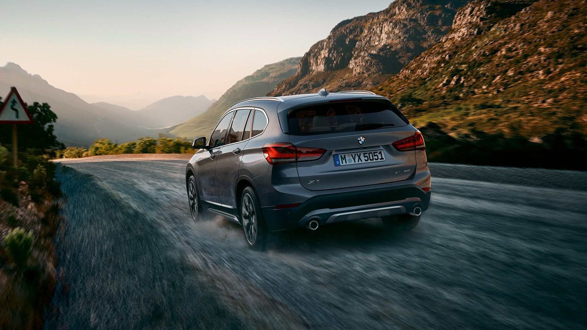 BMW X1, three-quarter rear view. BMW X1, three-quarter rear view driving in front of mountain scenery.