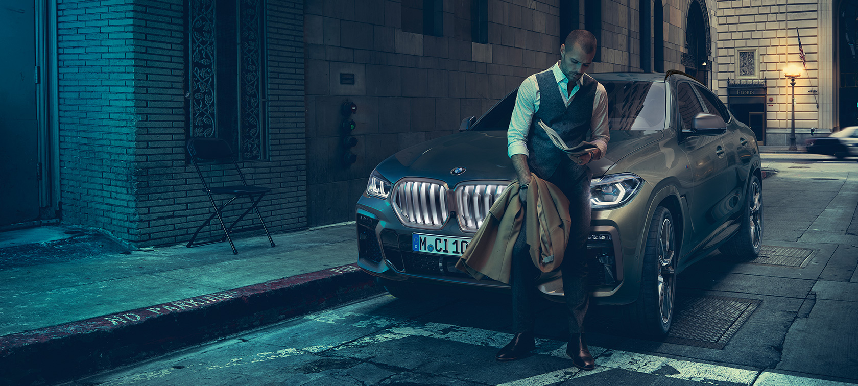 一名男士斜靠在 BMW X6 上。 一名男士斜靠在 BMW X6 上,側面視角,背景為都市環境。
